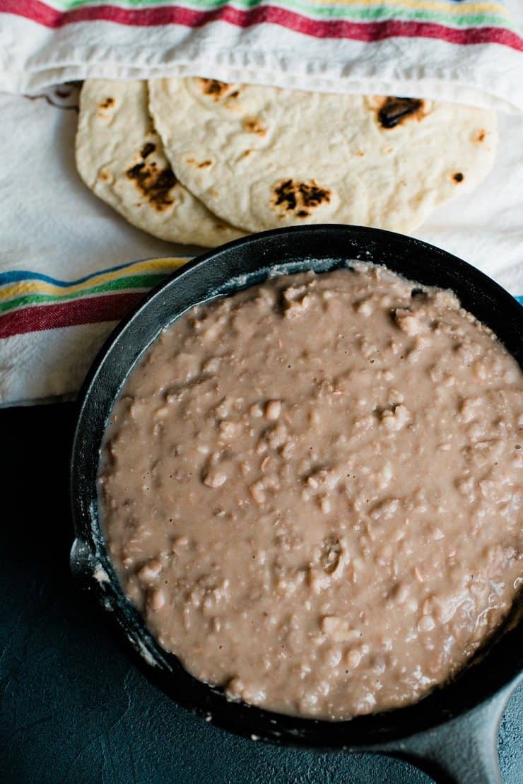 homemade refried beans in a cast iron skillet with flour tortillas 