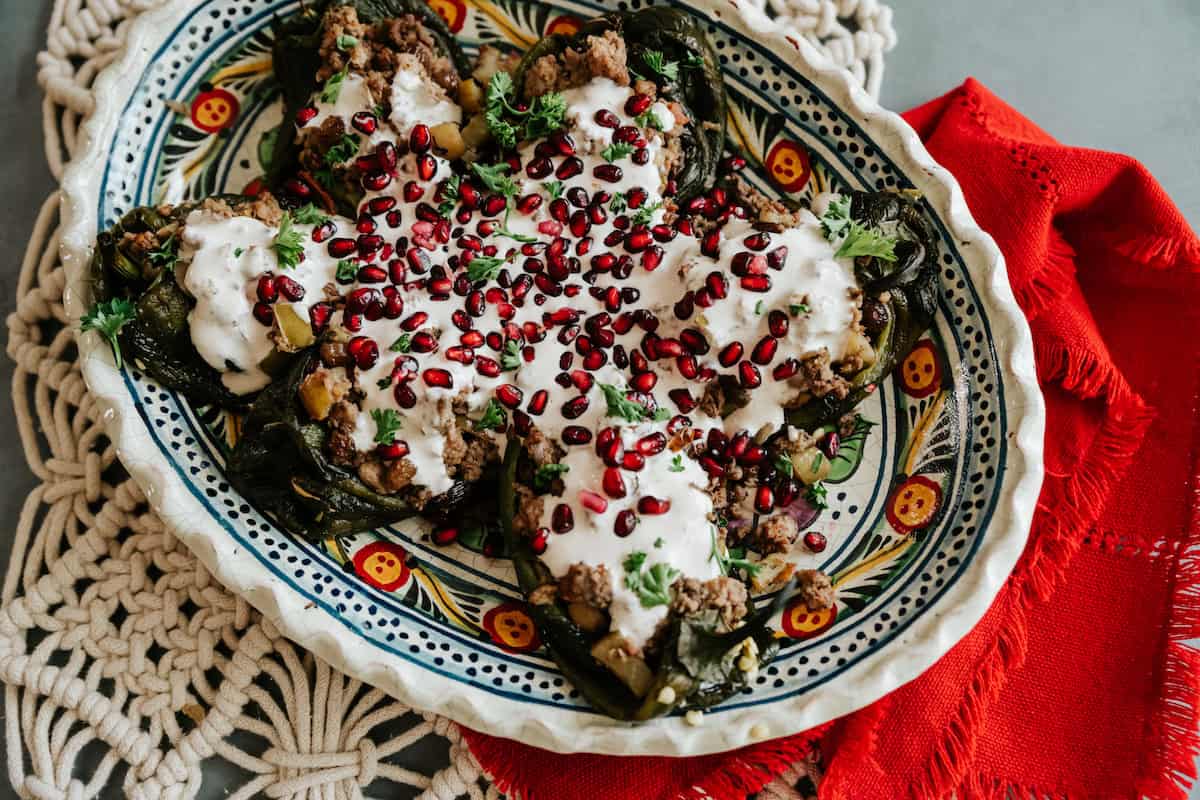 Traditional Chiles en Nogada on a ceramic serving platter with walnut sauce, fresh parsley, and bright red pomegranate seeds.