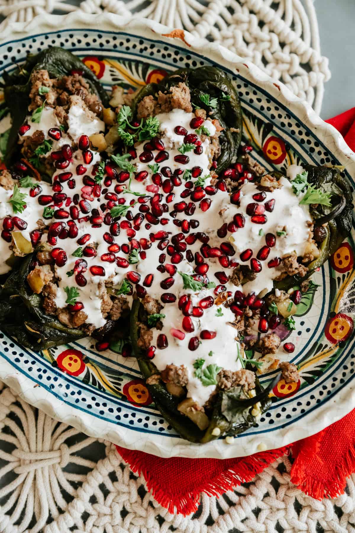 Overhead view of Chiles en Nogada on a colorful Mexican platter topped with creamy walnut sauce, pomegranate seeds, and parsley.