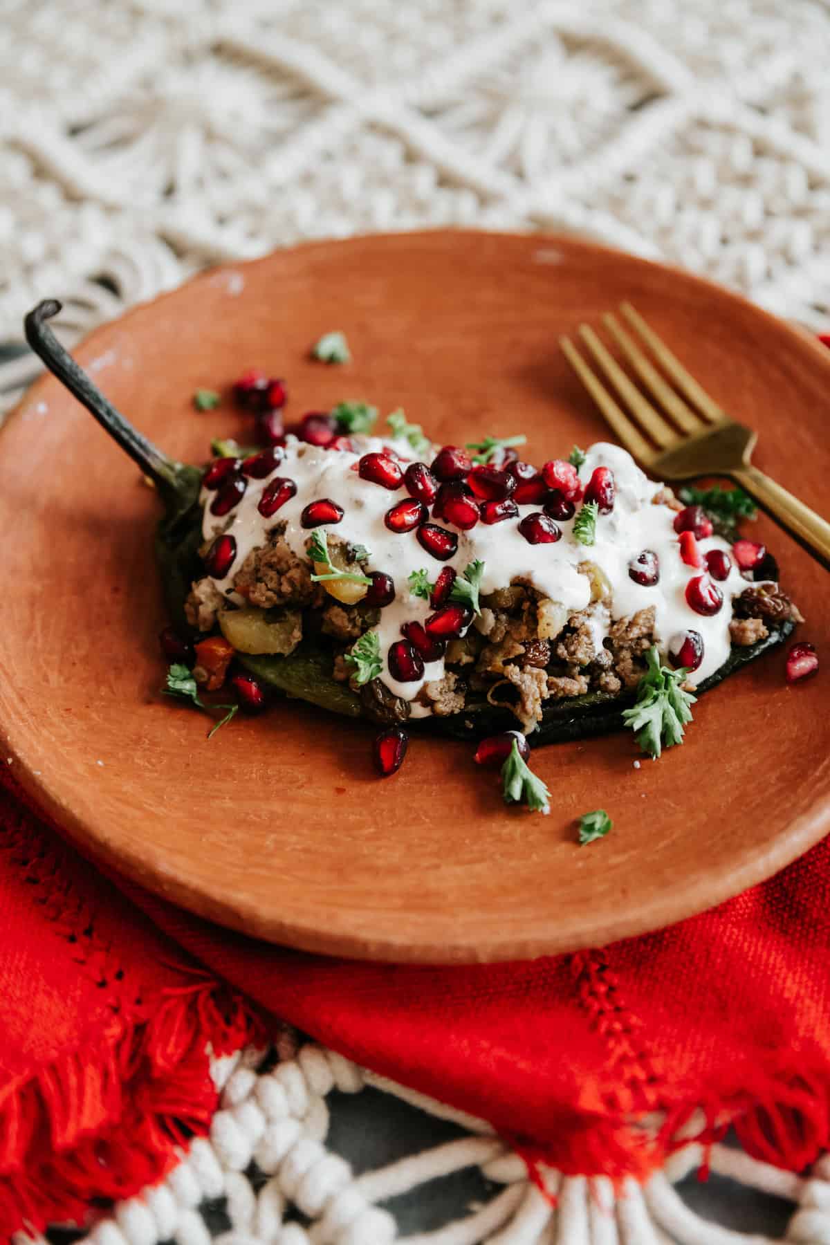 One serving of Chiles en Nogada on a terracotta plate topped with creamy walnut sauce, parsley, and pomegranate seeds.
