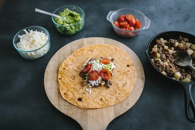 ingredients to make a crunchwrap at home wrap with ground beef, cheese, guacamole and tomatoes 