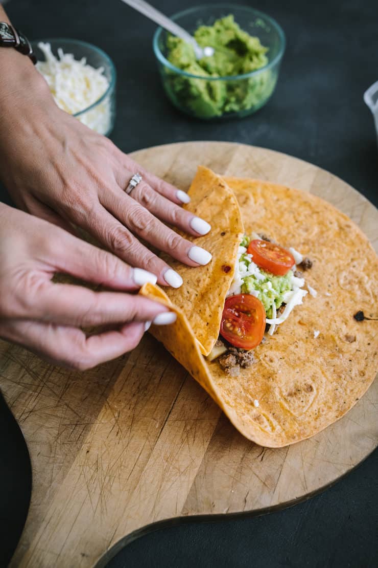 two hands beginning to fold a homemade crunchwrap on a wooden board