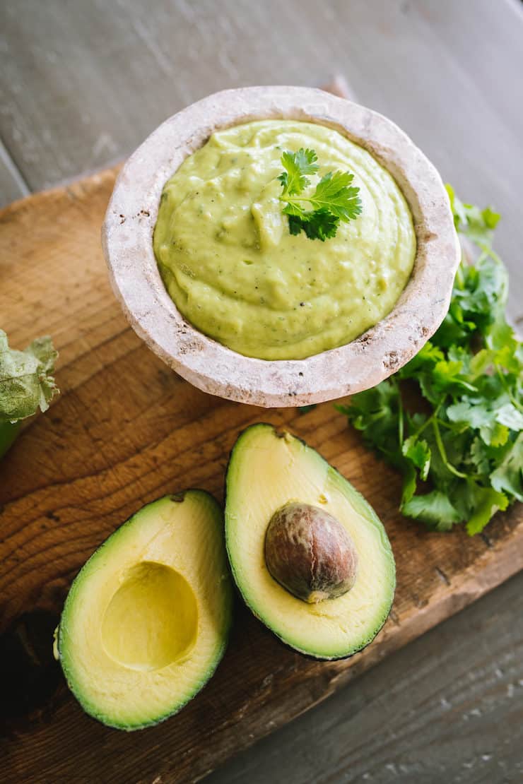 white mini molcajete filled with tomatillo avocado salsa or Guacamole Salsa with a side of avocados and cilantro 