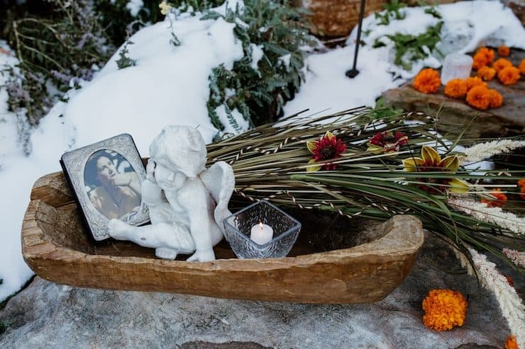 wooden bowl with a framed picture, a tea light candle, a small cherub statue, and marigolds to celebrate day of the dead