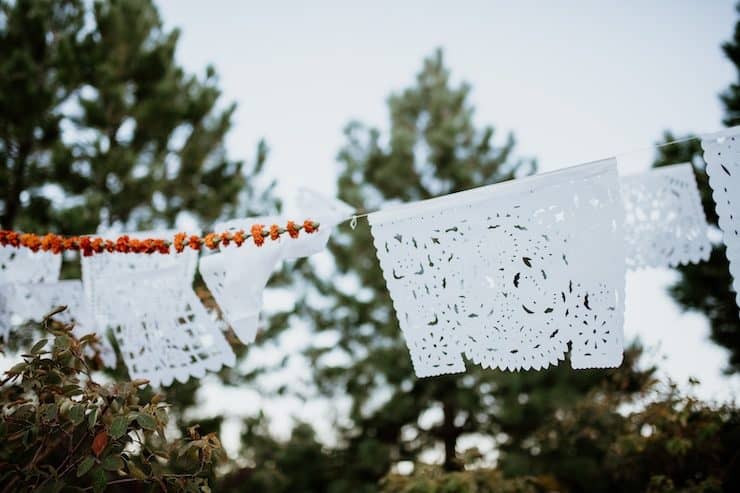 perforated decorated paper and marigolds strung up over a dia de muertos ofrenda