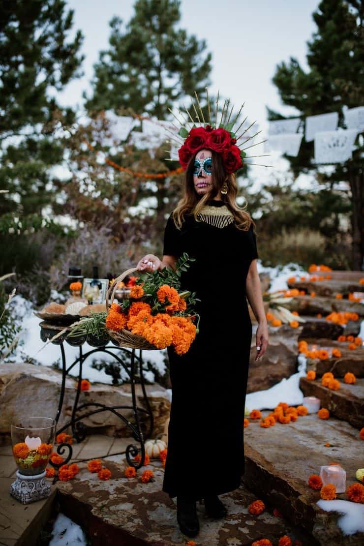 Calavera Catrina day of dead lady wearing black dress and red rose crown holding basket of marigolds