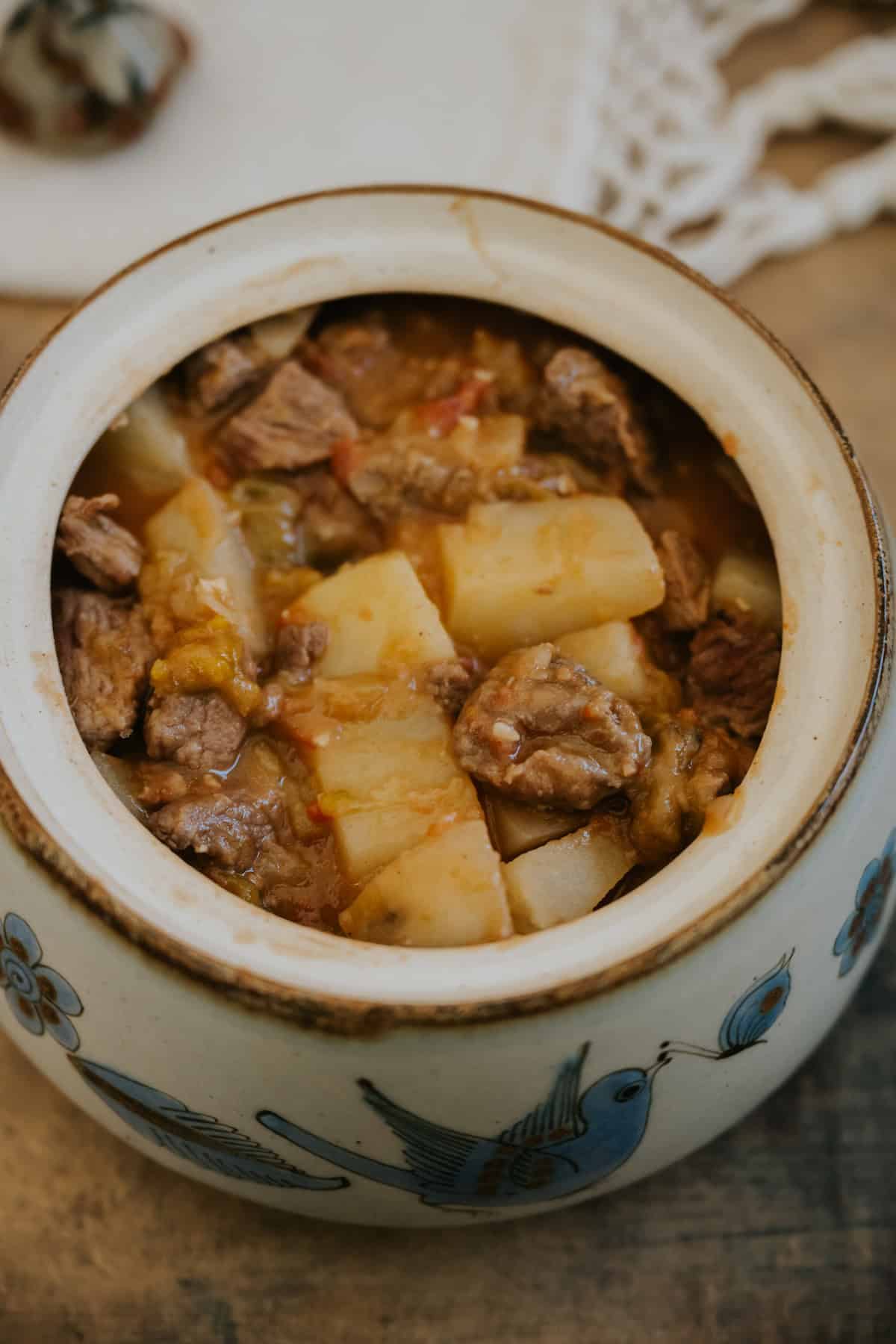 Close-up of tender beef and potatoes in chile verde sauce in a vintage platter.