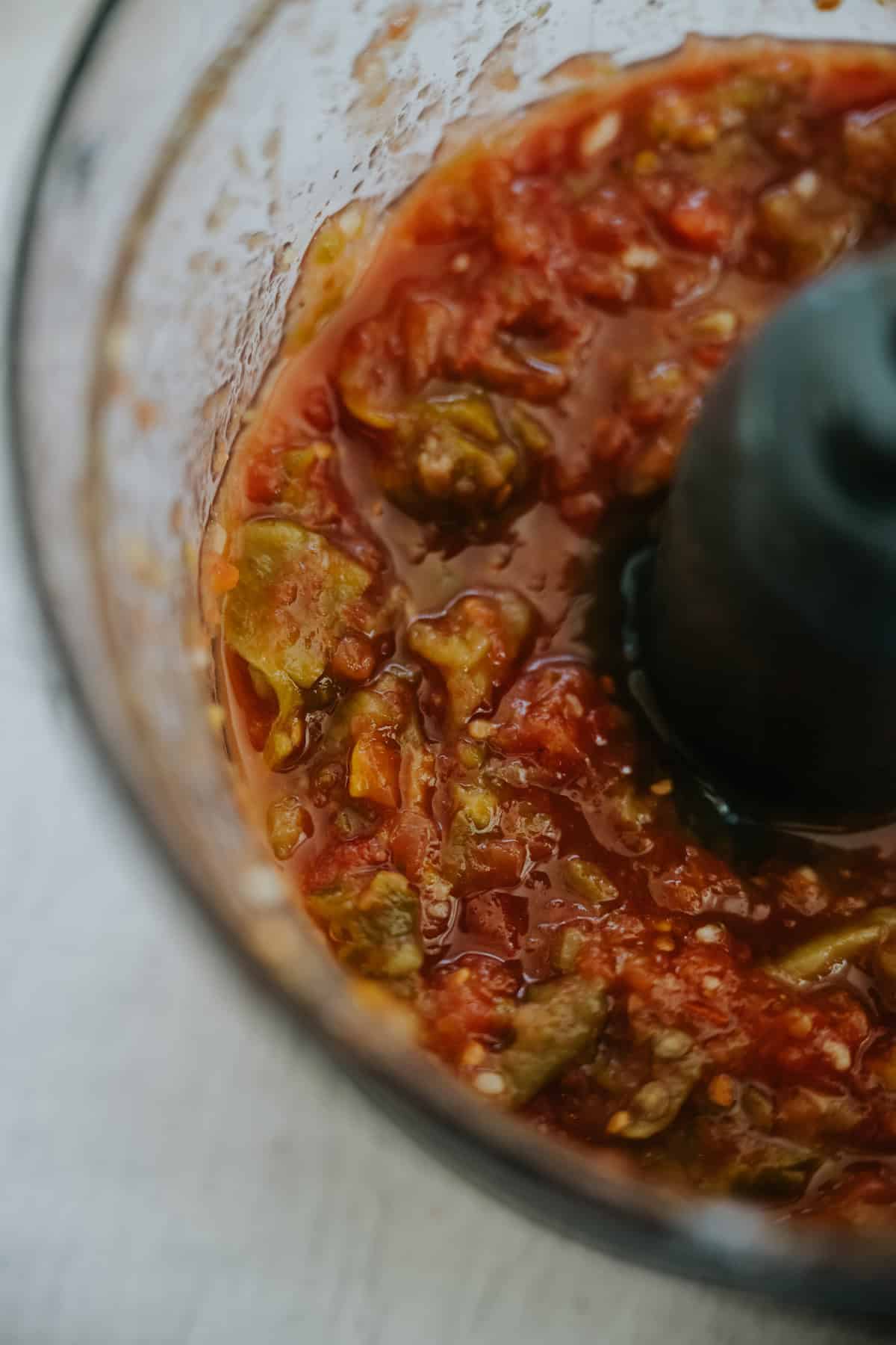 A food processor full of freshly pulsed green chile, tomato, and garlic salsa used in the chile verde recipe.