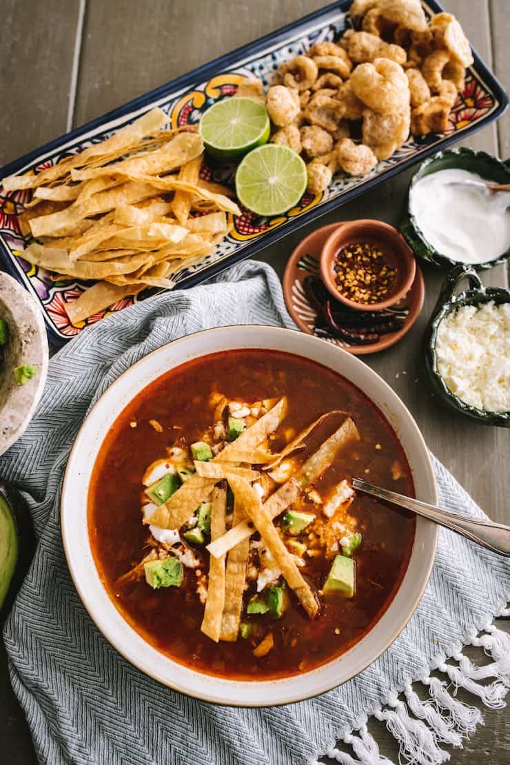 Classic chicken tortilla soup in a white bowl with an assortment of toppings on a platter nearby