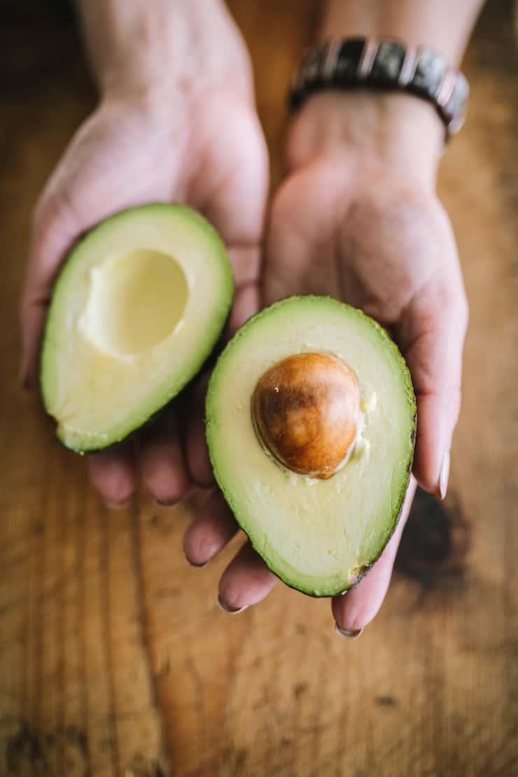 hands holding two halves of an avocado