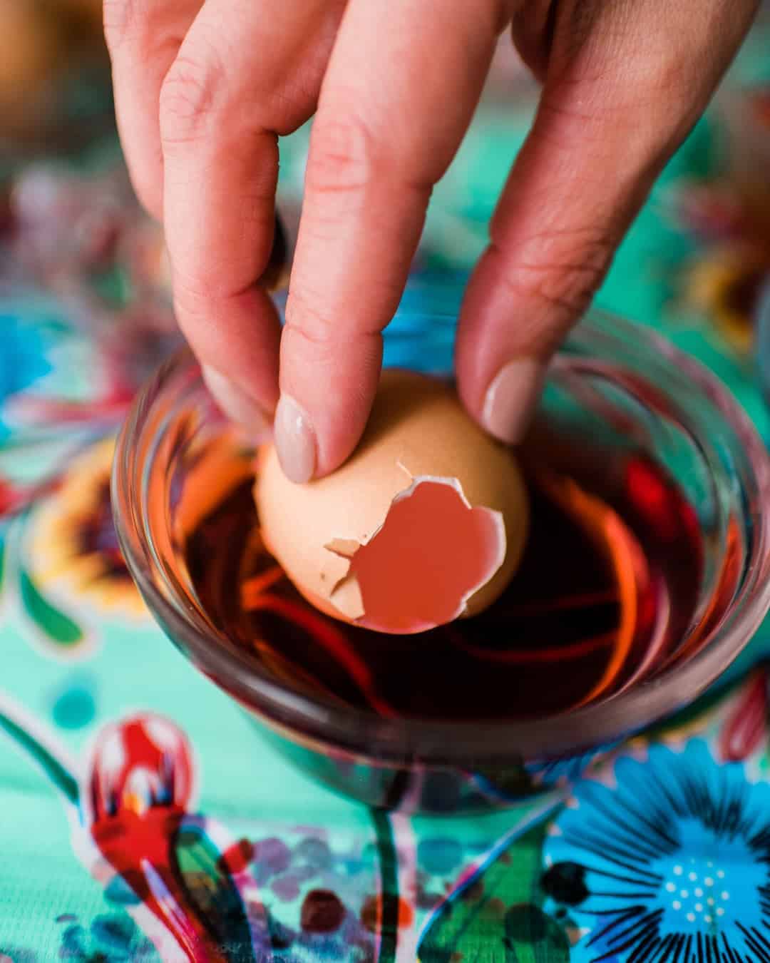 brown egg shell with hole on top being dipped into easter egg dye.