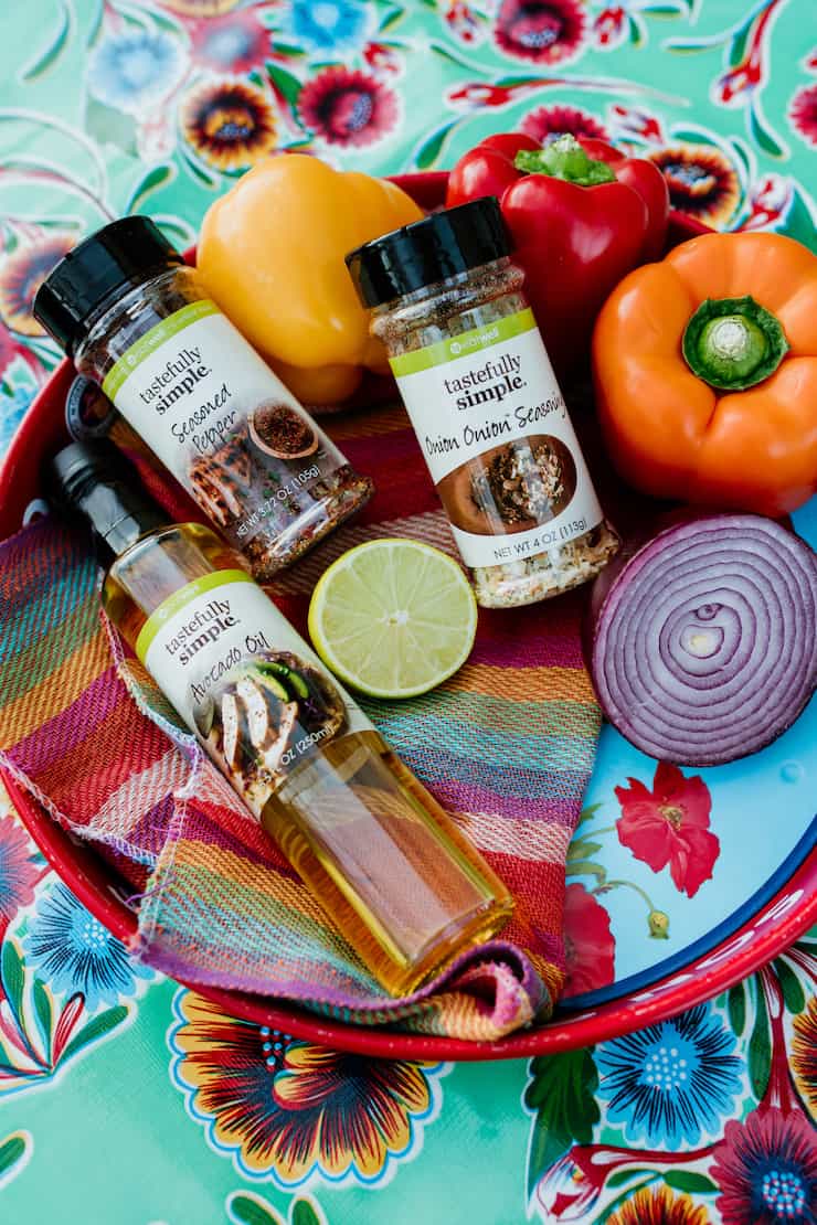 tastefully simple avocado oil and seasonings in a platter with colorful bell peppers lime and red onion on a colorful Mexican tablecloth 