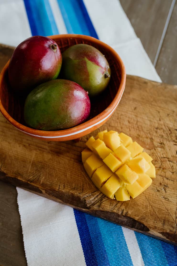 bowl of three mangos on a cutting board with a halved and cubed mango