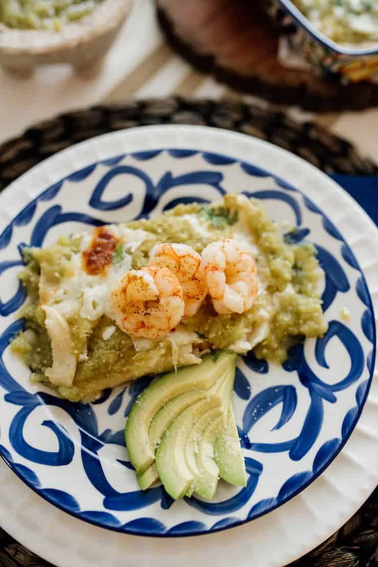 a serving shrimp enchiladas in a salsa verde with a side of slices of avocado 
