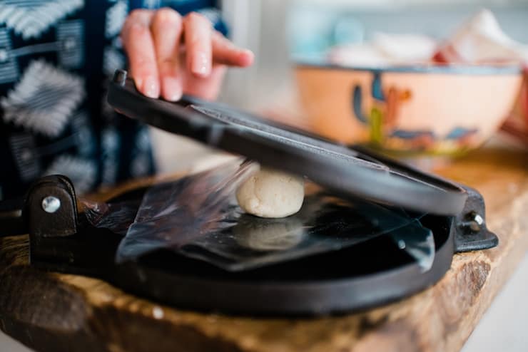 Tortilla press with a ball of dough being pressed in between to make corn tortillas 