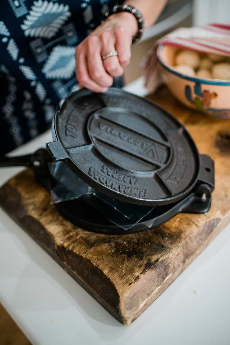 Cast Iron Tortilla Press on a wooden cutting board with a bowl in the background filled with dough balls to make corn tortillas