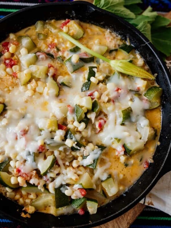 Creamy calabacitas (Mexican-style zucchini with corn) topped with melted Chihuahua cheese in a cast iron skillet, made with fresh zucchini, sweet corn, tomatoes, and onions.
