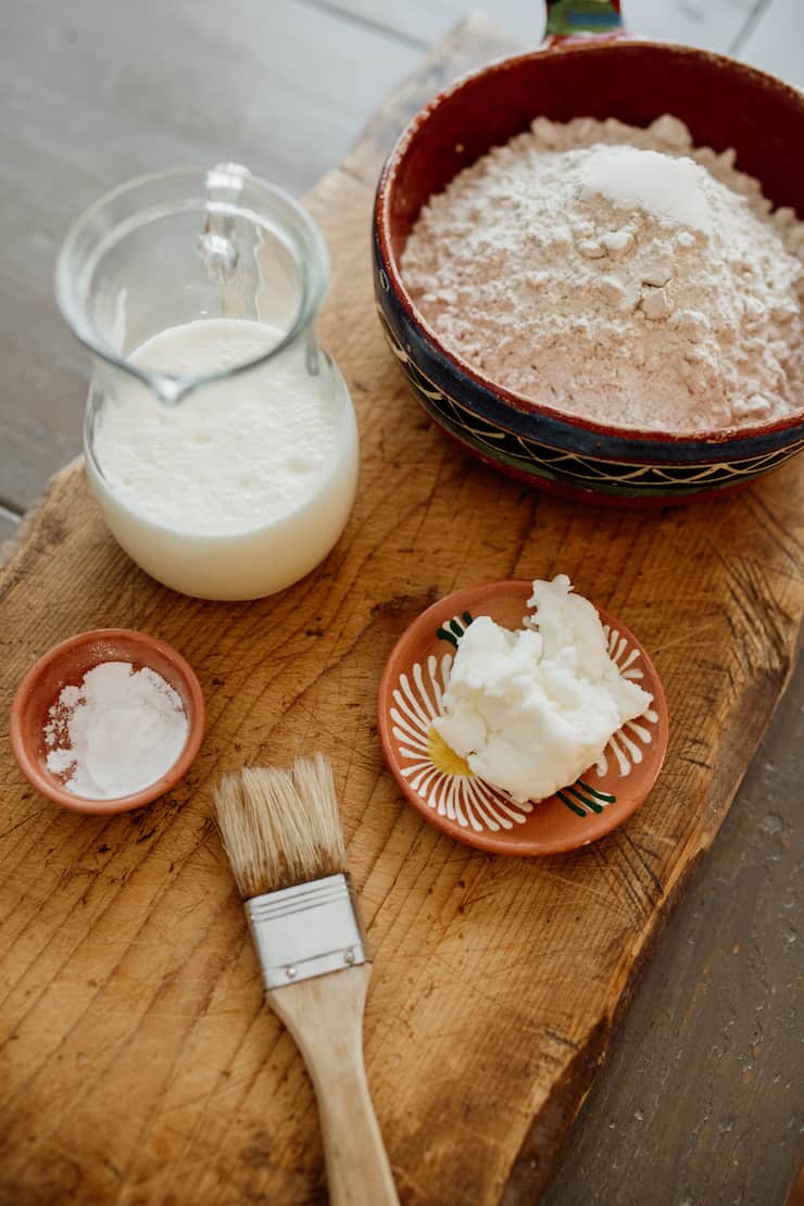 suero (buttermilk), baking powder, shortening, flour and a pastry brush on a wooden board
