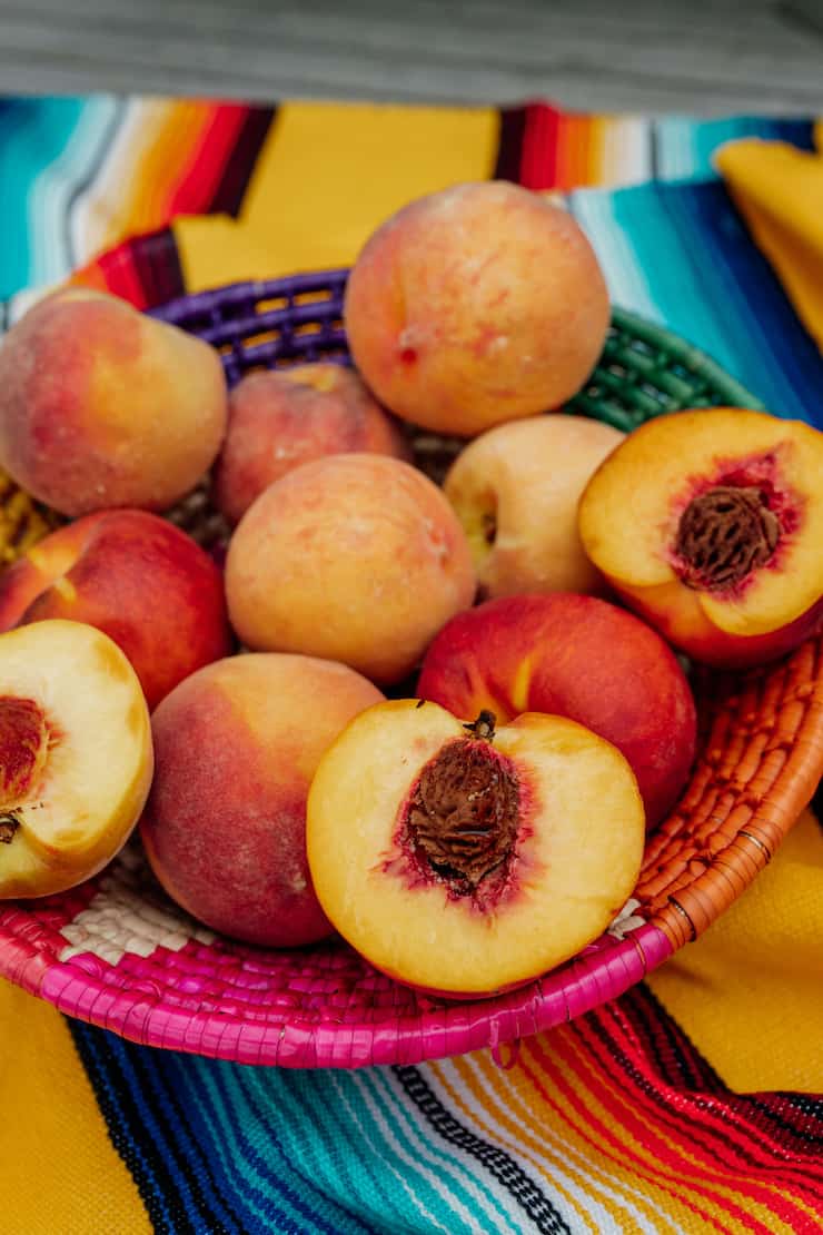 multicolored basket filled with peaches, some of which are halved