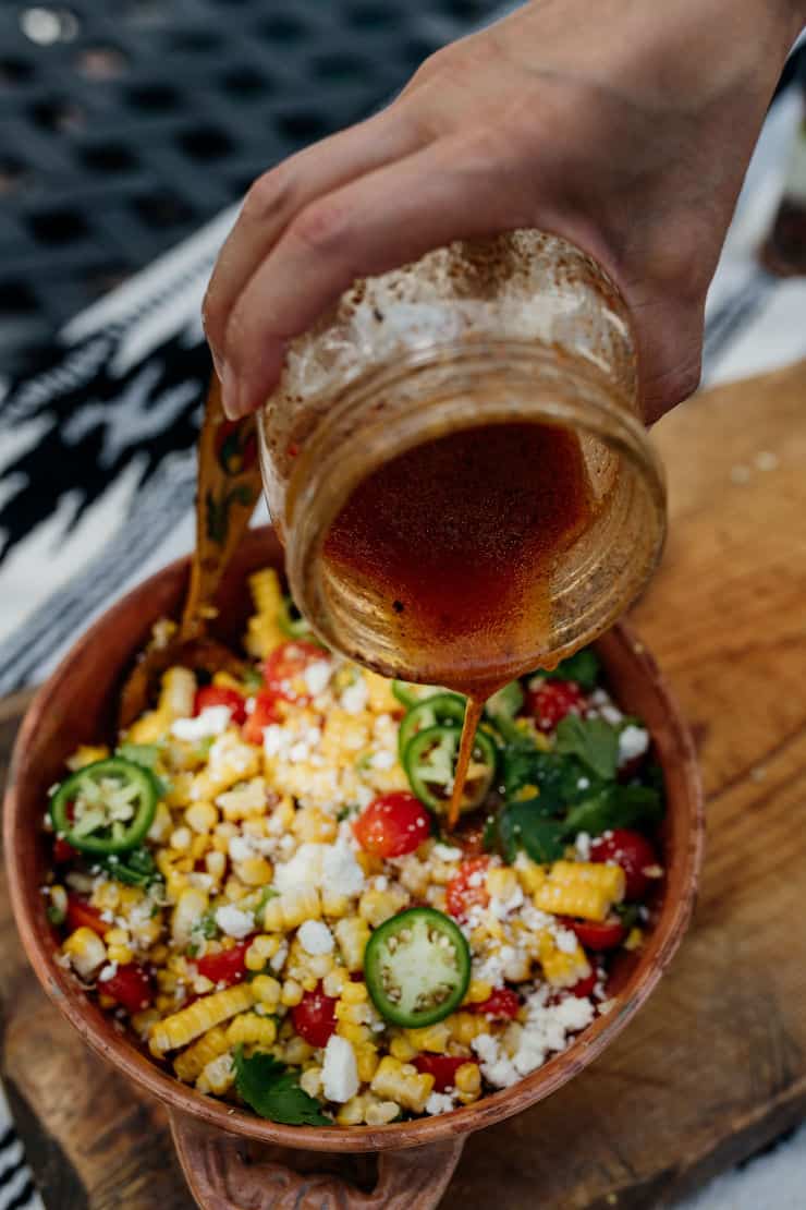 hand holding a mason jar and drizzling dressing on Mexican street corn salad