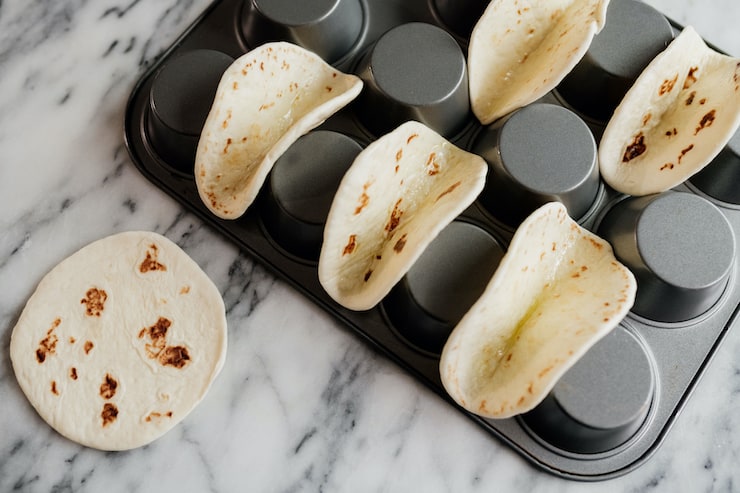 mini flour tortillas on a flipped muffin tray on a marble surface ready to bake