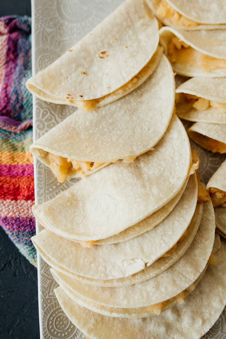 potato tacos on a white platter ready to be fried.