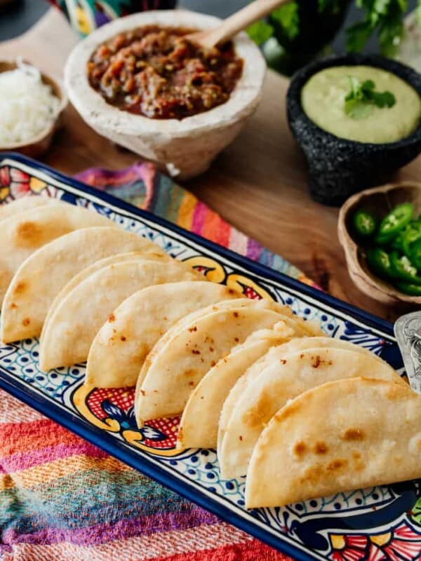 Crispy Potato tacos served on a long tray with plenty of sides next to it