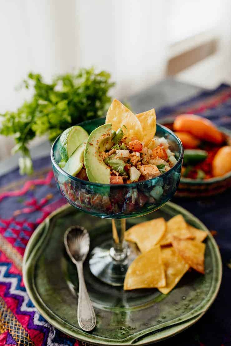 ceviche style canned salmon salad in a ceviche glass on a green plate with tortilla chips and avocade