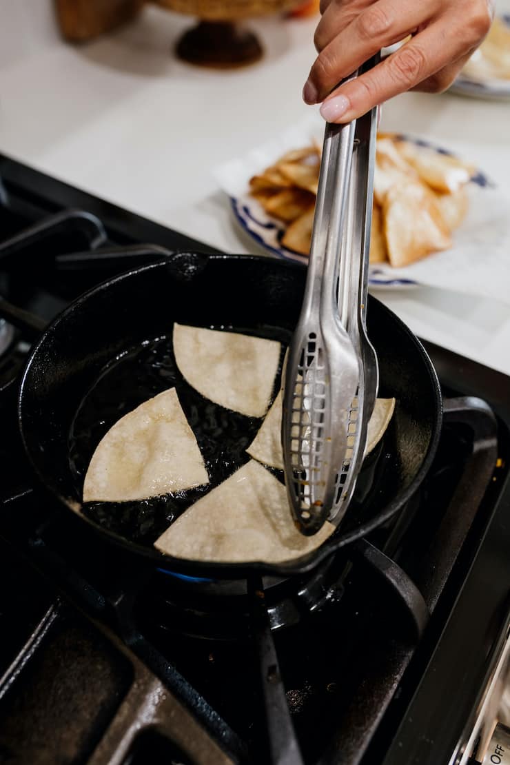 hand holding tongs for flipping tortilla quarters in a cast iron pan with oil.