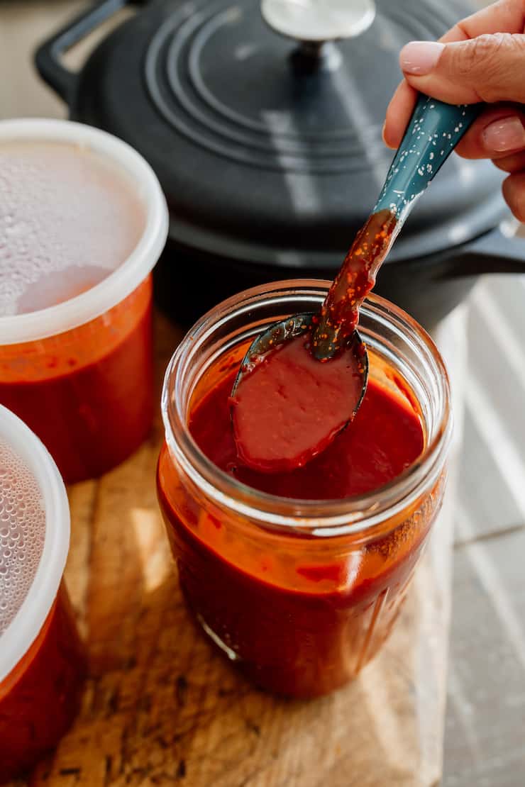 Red Chile sauce in a mason jar with a teal spoon and black iron pot in background 