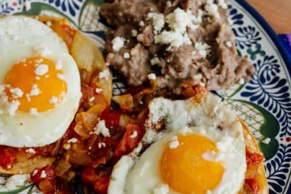 plate of huevos rancheros with a side of refried beans on a blue and white plate