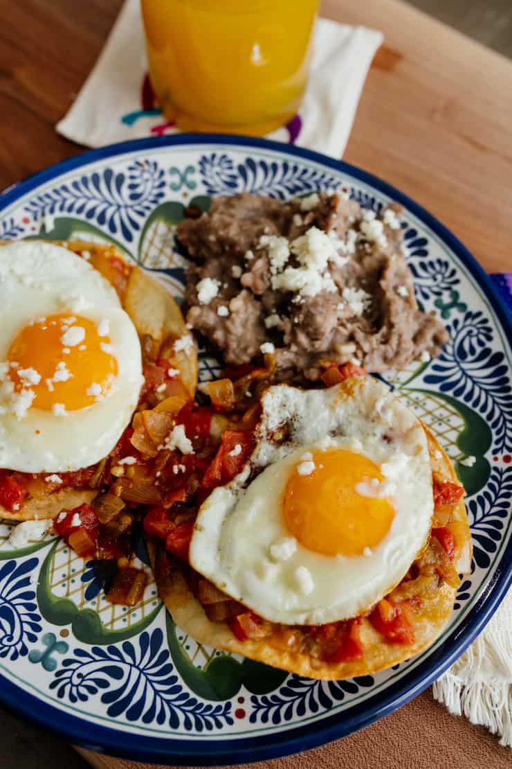 huevos rancheros on a blue and white plate with refried beans and two sunnyside up eggs