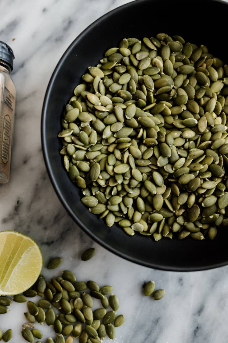 raw pepitas, also known as pumpkin seeds, in a black bowl on a marble countertop