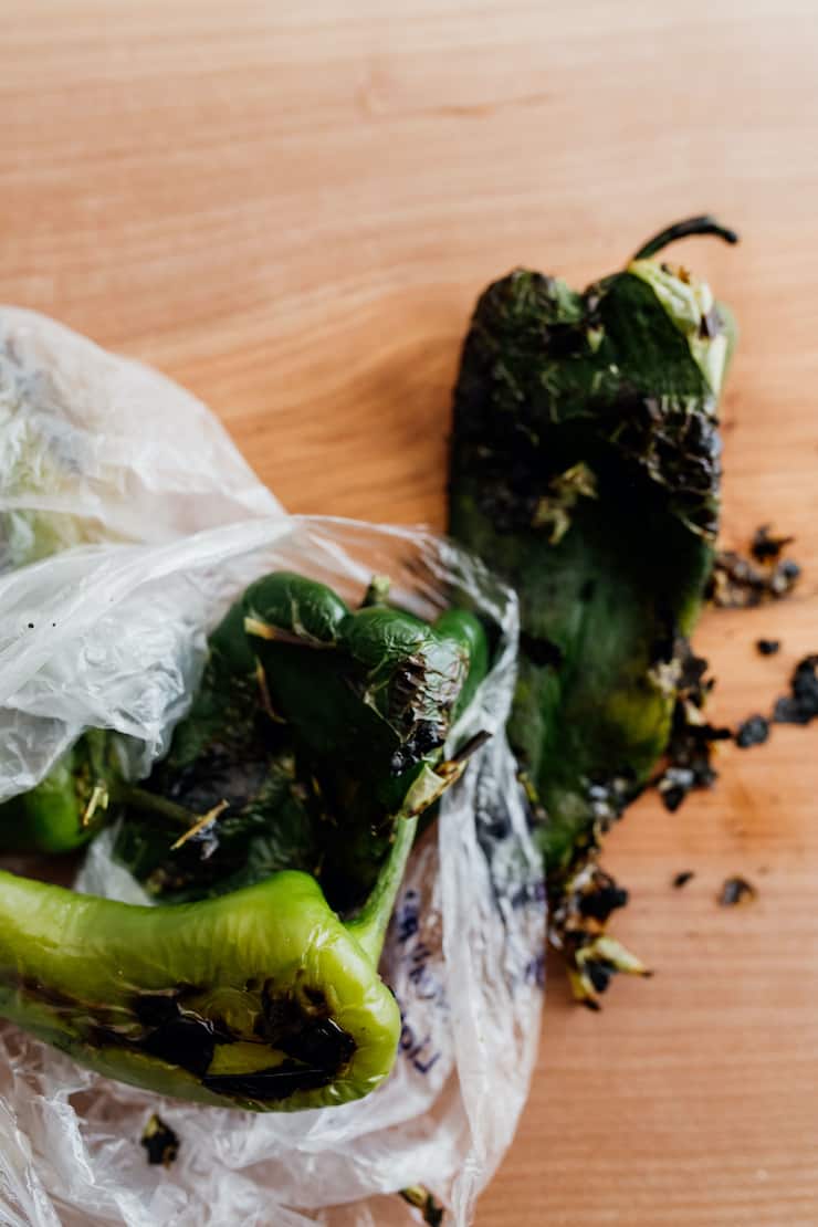 poblano peppers that have been roasted are placed in a plastic bag to steam to aid in removing the skins