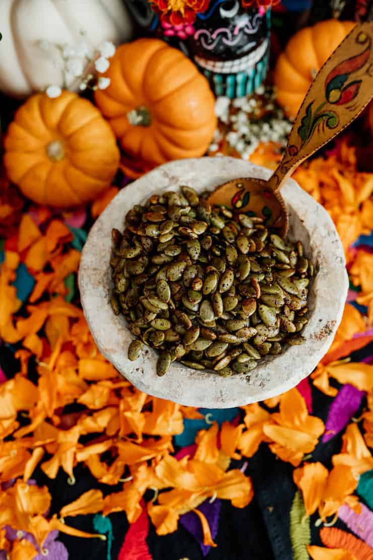 spicy roasted pepitas in a stone bowl with a painted wood spoon on a dia de muertos offrenda