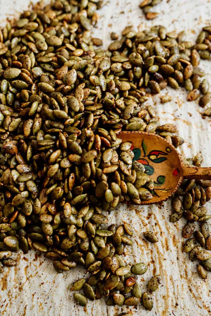 close up shot of roasted pepitas on a parchment lined sheet pan with a wooden spoon