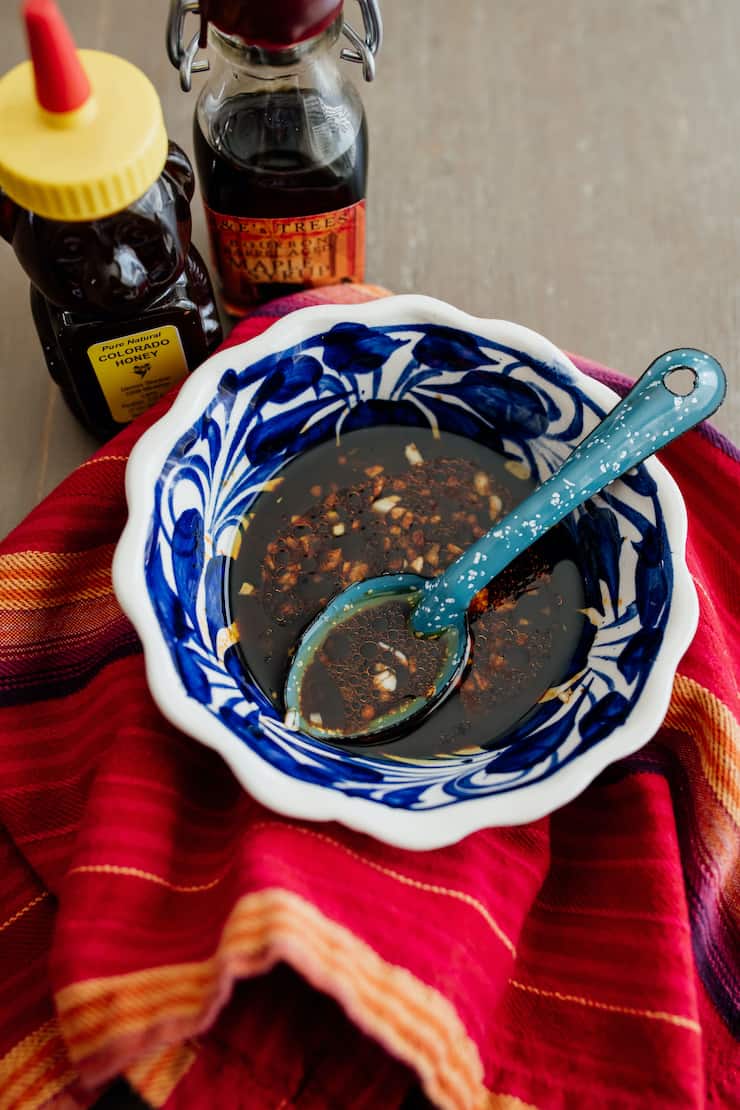 spicy sweet dressing for winter salad in a blue and white bowl on a red tea towel with a jar of honey and hot sauce behind it