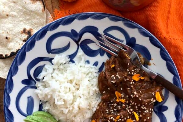 chicken mole on a blue and white plate with white rice and salted avocado