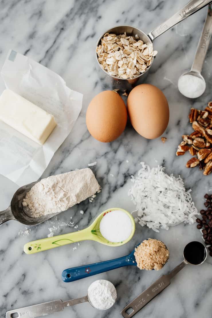 butter, flour, eggs, salt, leavening, brown sugar, vanilla, coconut shreds, oats, chopped pecans, chocolate chips and vanilla as mis en place for cowboy cookie recipe