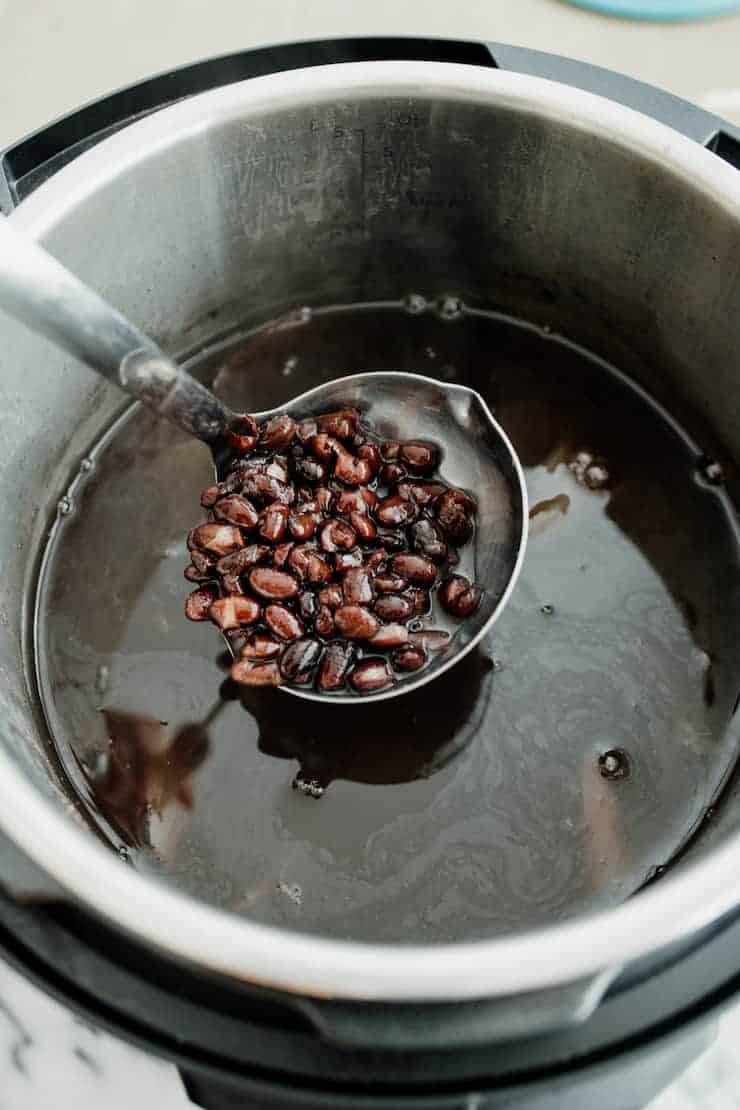 ladle holding a scoop of black beans from the insert of an Instant Pot