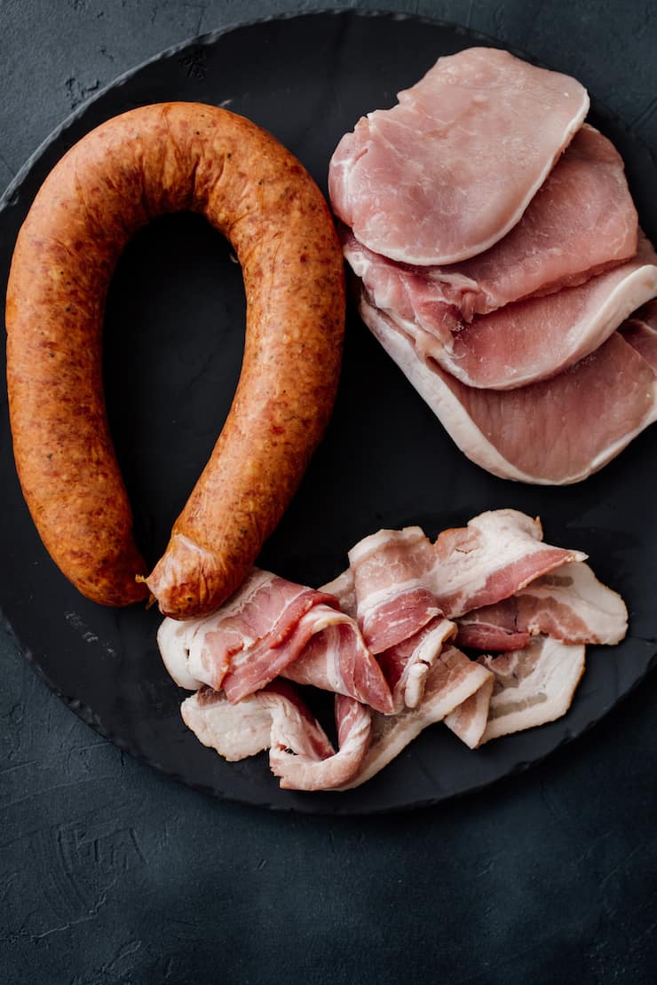 meats for making Brazilian feijoada on a black slate surface.
