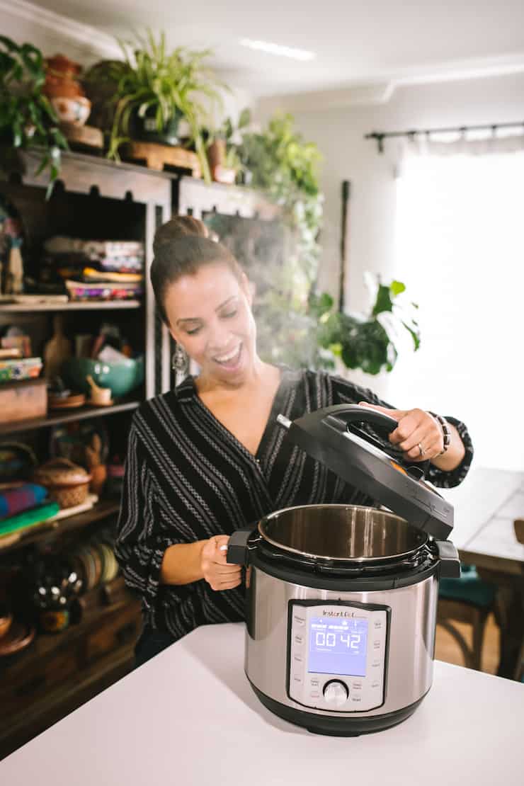 latina woman removing the lid of an instant pot with a big smile on her face