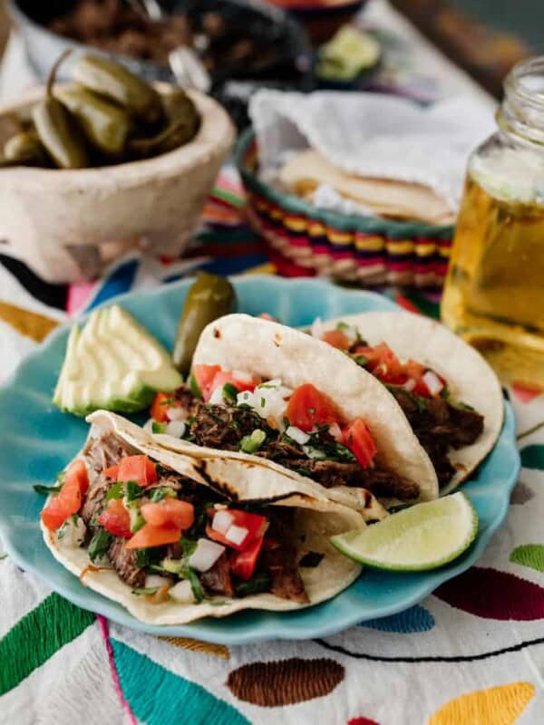 three slow cooker brisket tacos on a turquoise plate topped with pico de gallo and carne deshebrada