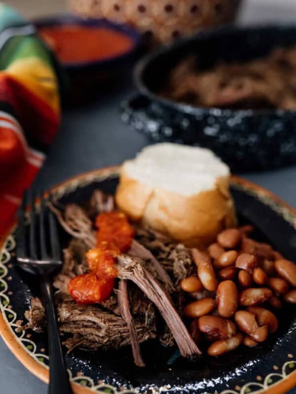 shredded crockpot brisket on a black plate with beans, bolillo and salsa