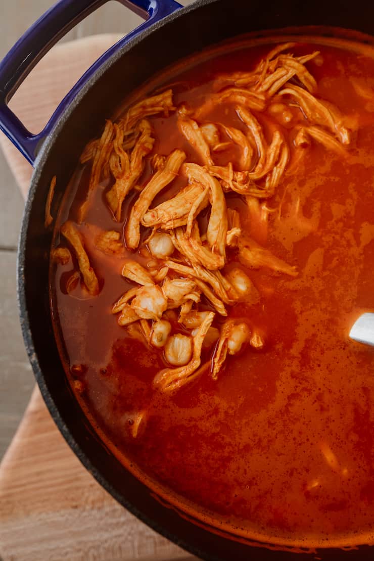 overhead shot of red chicken pozole in black dutch oven