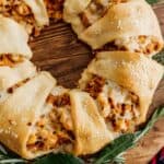 Chorizo and Egg Breakfast Wreath made with crescent dough, filled with chorizo, scrambled eggs, and melted cheese, baked golden brown and garnished with bay leaves and fresh herbs on a wooden board.