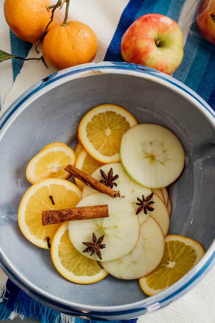 thin slices of apples and oranges in a ceramic bowl with star anise and cinnamon sticks