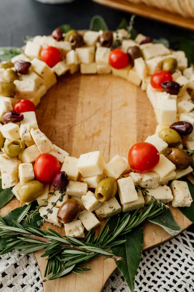 close up of a christmas wreath style savory cheese board on a wooden tray