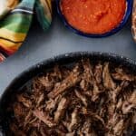 crockpot slow cooker brisket in a black serving bowl with chile de arbol salsa on the side.