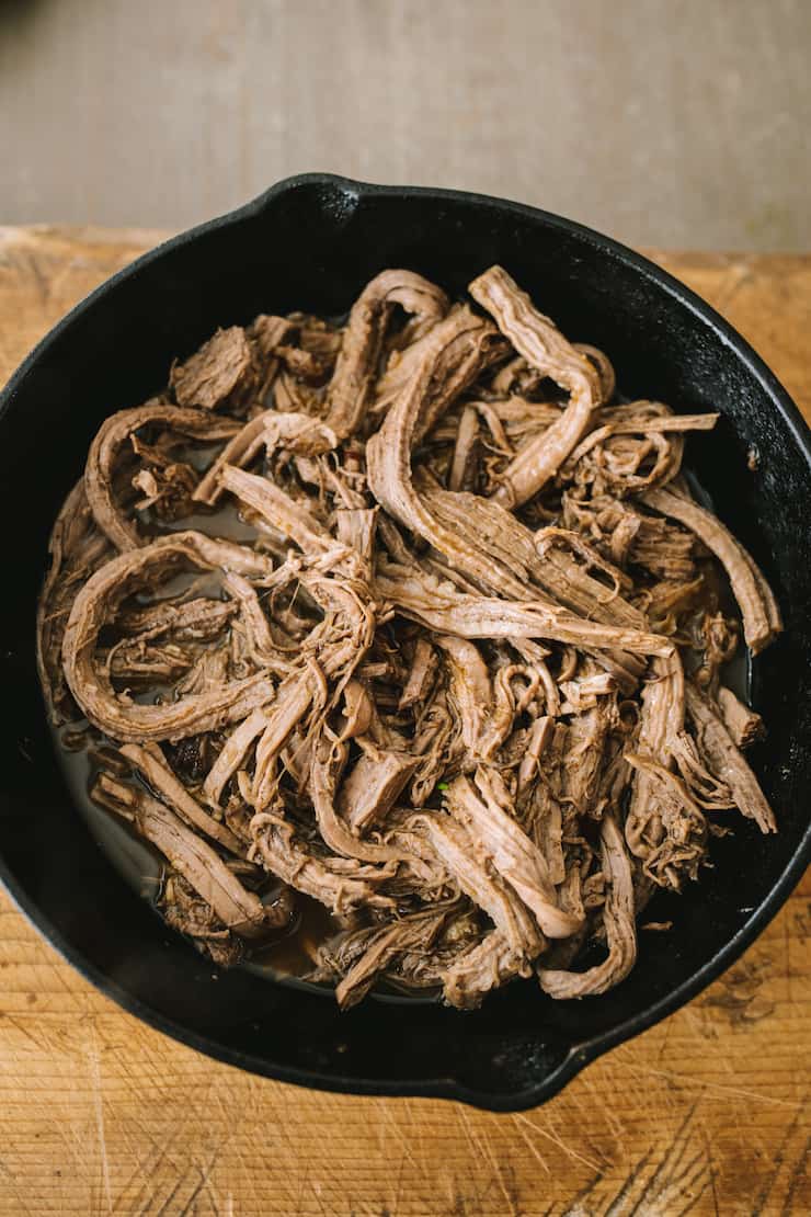 shredded slow cooker beef brisket and juices in a cast iron skillet on a wooden table